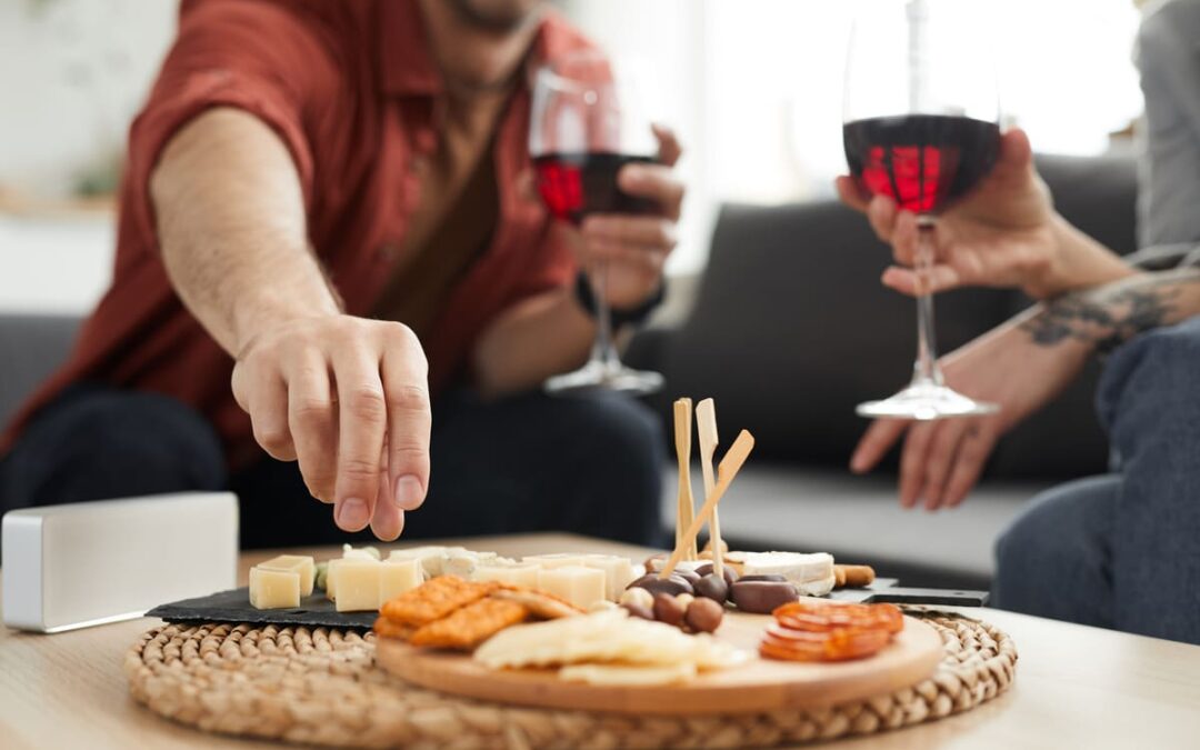 people holding red wine in glasses snacking on a cheese plate