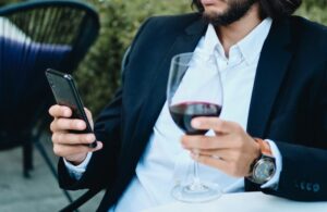 confident-latin-businessman with glass of wine using cellphone sitting on outdoor table